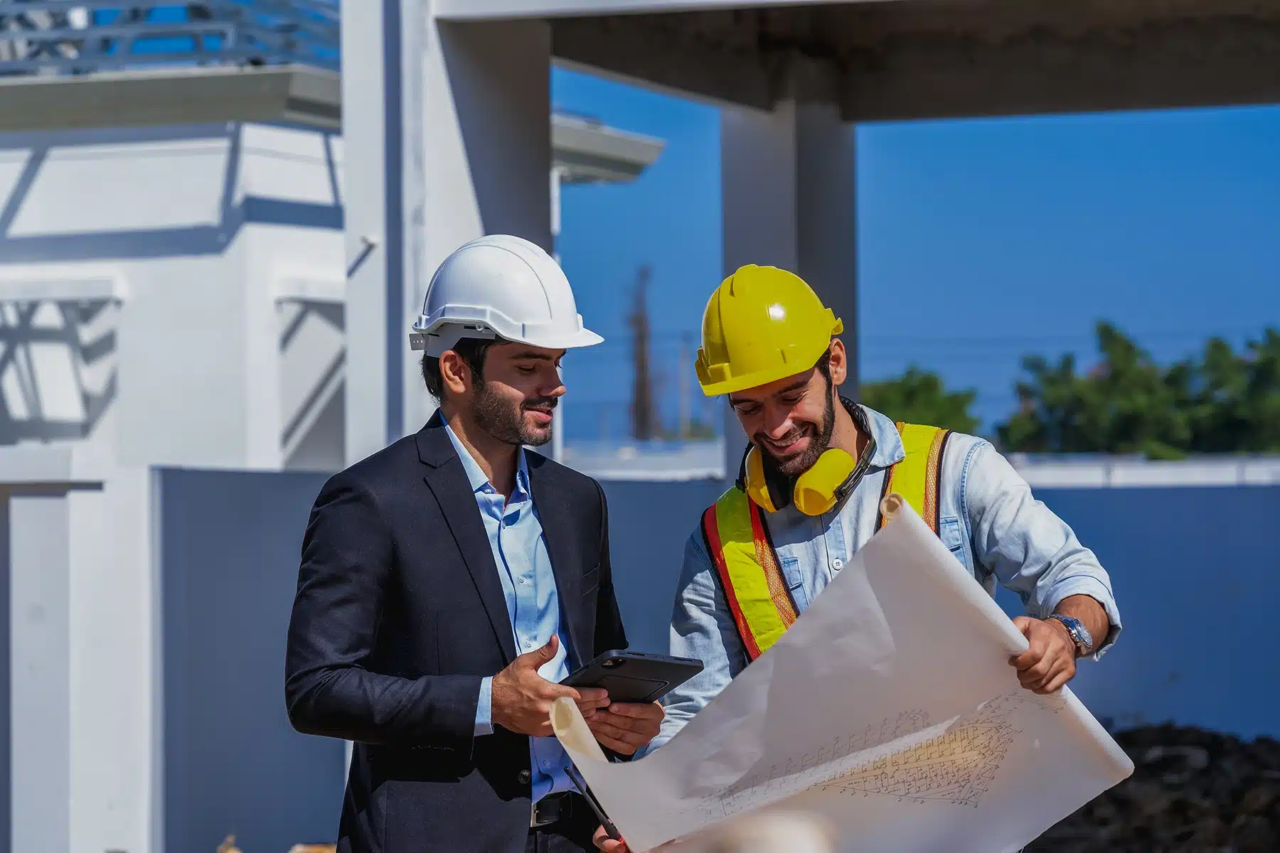 Ein Geschäftsmann und ein Bauarbeiter stehen auf einer Baustelle und schauen gemeinsam einen Bauplan an.