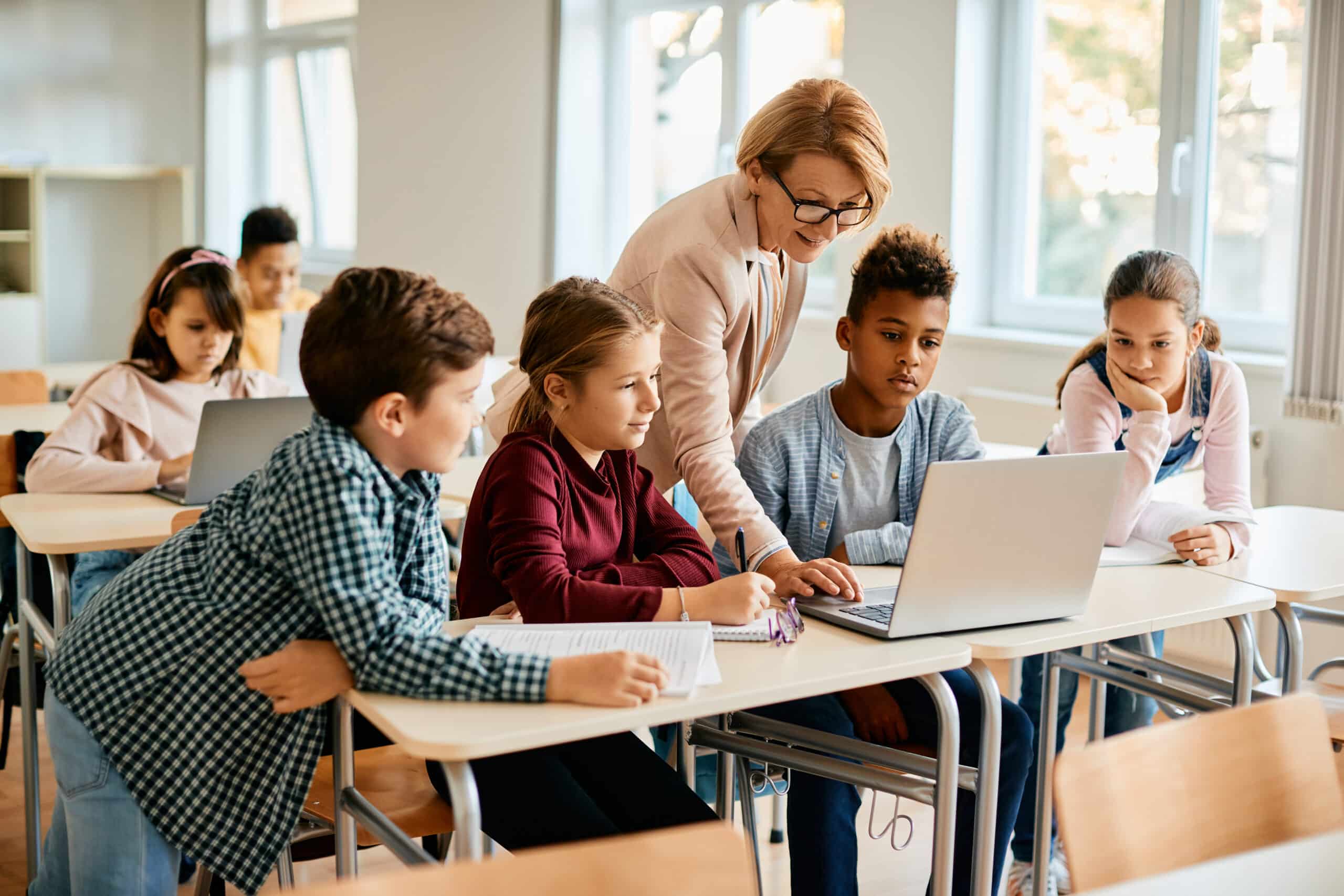 Eine Gruppe von Grundschülern hat mit ihrem Lehrer im Klassenzimmer Computerunterricht.